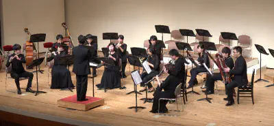 第3.5回演奏会のステージの様子。13人の管楽器奏者が指揮者を中心として半円形に並び、《13管楽器のためのセレナード》を演奏している。